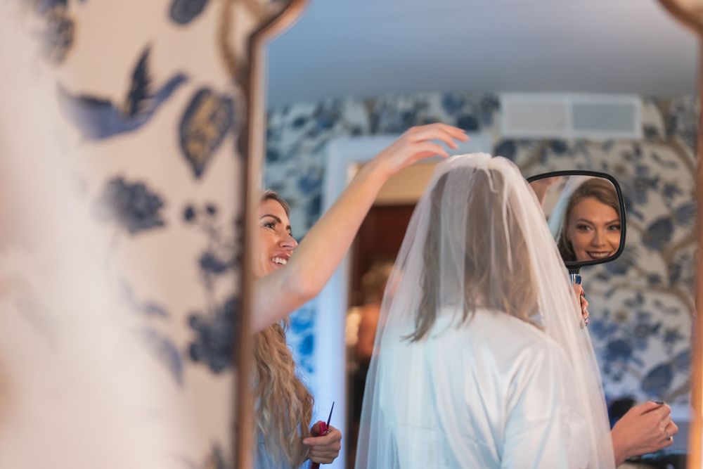 Getting ready moment with bride in white dress and veil being assisted.