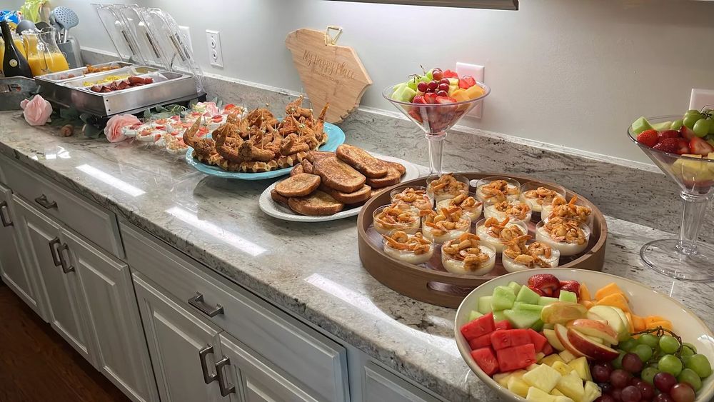A panoramic view of a buffet spread featuring appetizers, shrimp platters, and fresh fruit on a marble countertop.