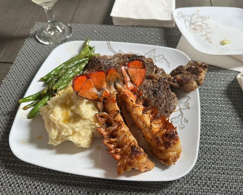 Surf and turf dinner plate with grilled steak, lobster tail, glazed carrots, asparagus and mashed potatoes on white plate.