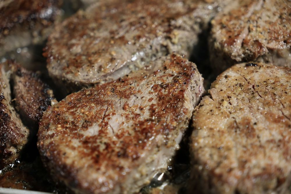 Pan-seared meat patties or cutlets cooking in a skillet with a golden brown crust.