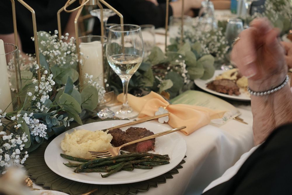 An elegant table setting with eucalyptus greenery, white candles, and a plated meal with wine glasses.