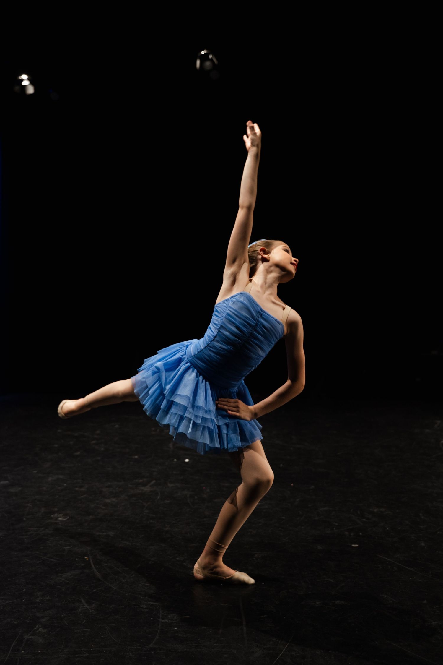 Ballet dancer in blue tutu performs dynamic leaps and poses in sequence against dark backdrop.