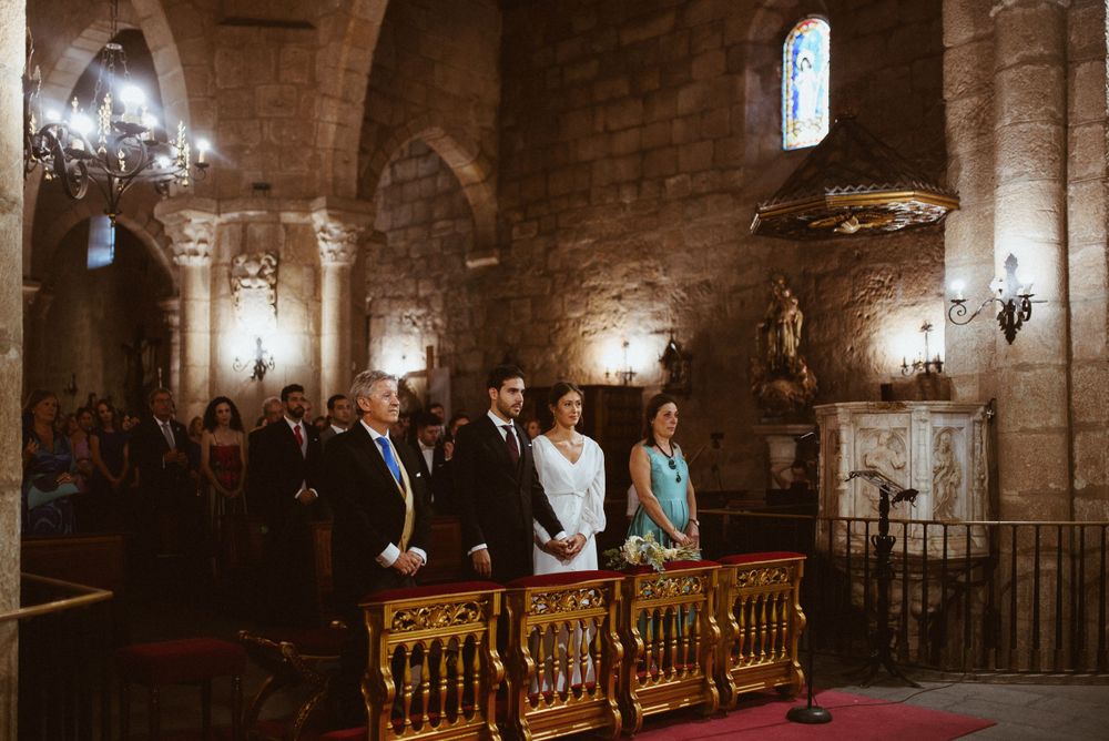 Wedding ceremony in progress inside candlelit stone church with guests seated.