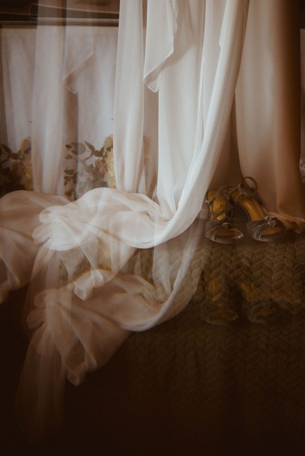 Flowing white curtains and gold shoes create an elegant wedding detail shot.