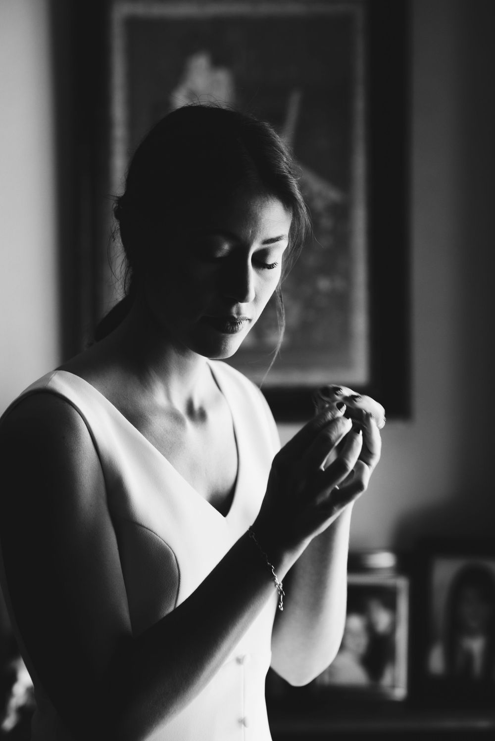 A dramatic black and white portrait of a bride in white dress looking down in contemplative pose.