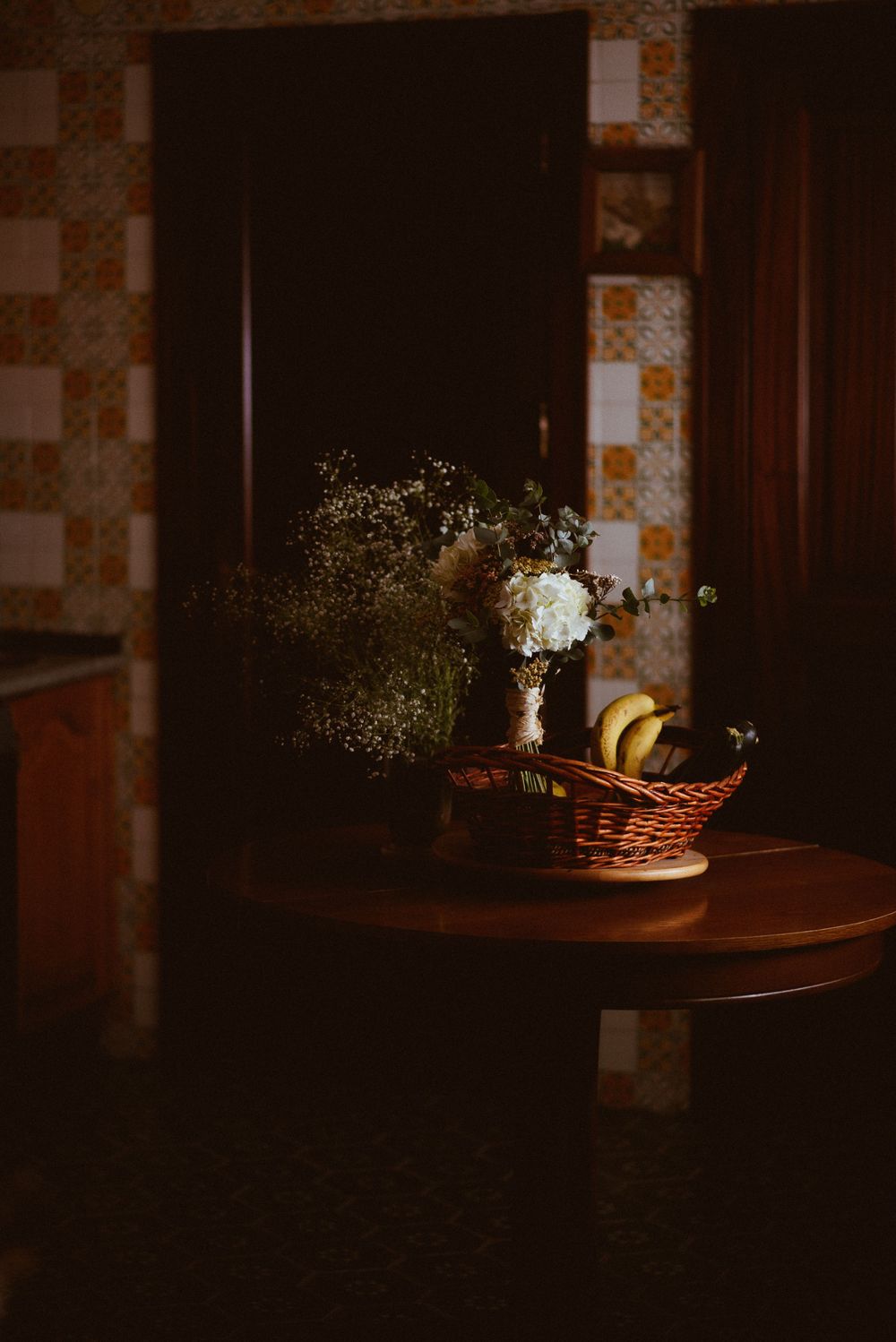 A moody still life of flowers in a vase on a round table with vintage wallpaper.