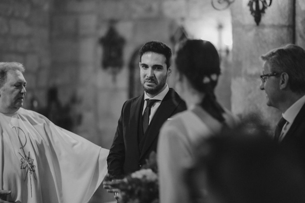 Church wedding ceremony with priest and wedding party in stone chapel.