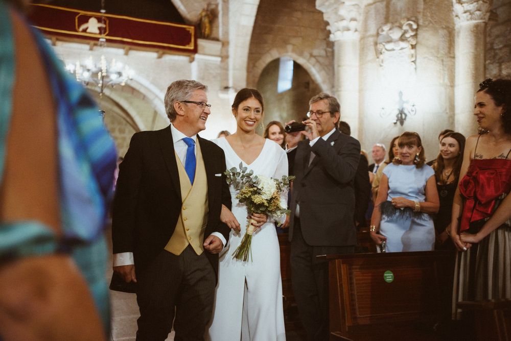 Wedding ceremony procession in traditional stone church with guests watching.