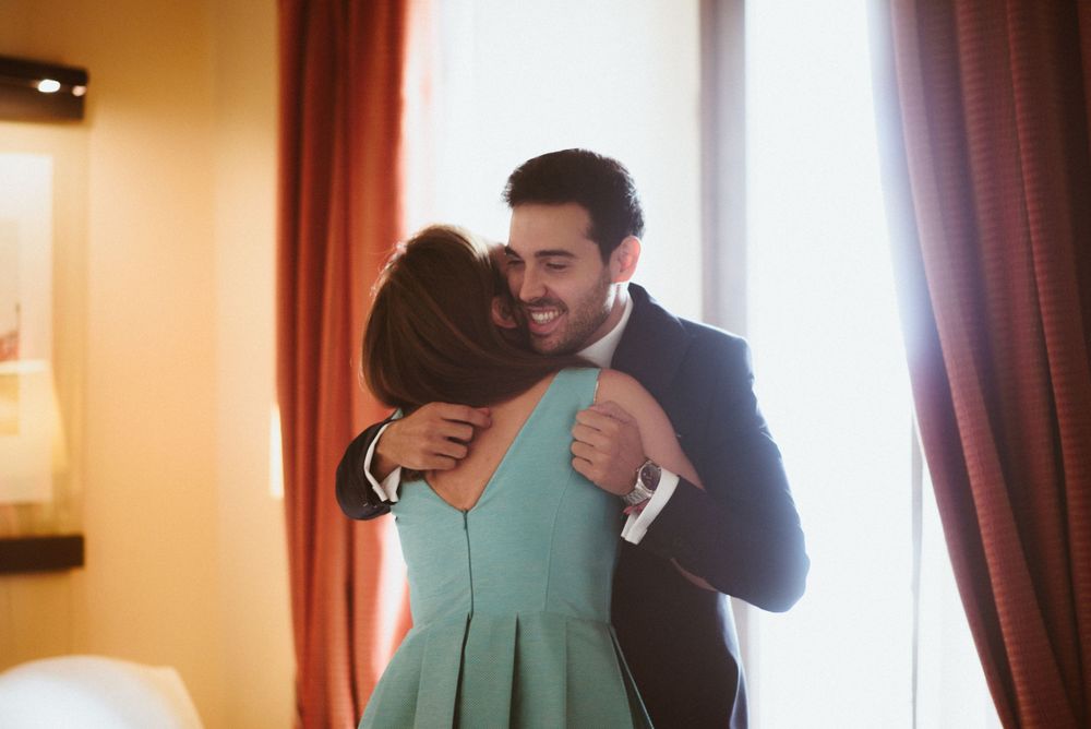 A couple shares a joyful embrace in a warmly lit room with red curtains.