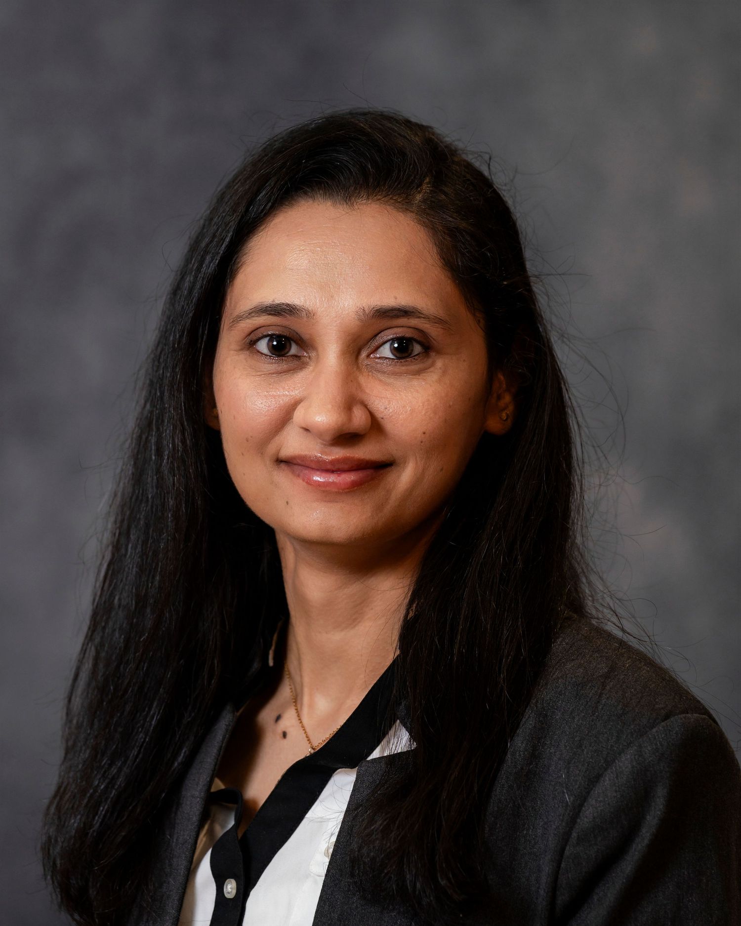 Corporate headshot against dark gray backdrop showing black blazer and white collared shirt.