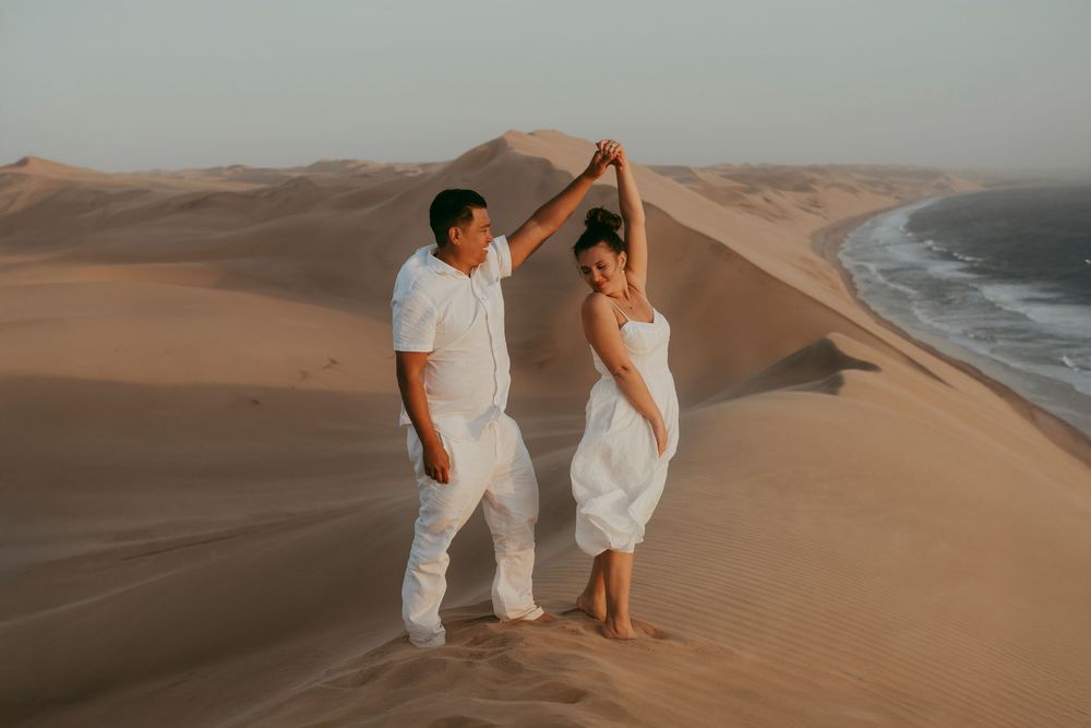 A surprise proposal unfolding on top of a dune in Sandwich Harbour, with the woman reacting emotionally as the sun sets behind them.