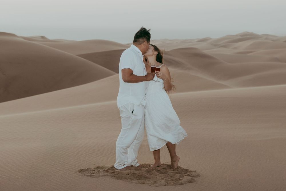 A surprise proposal unfolding on top of a dune in Sandwich Harbour, with the woman reacting emotionally as the sun sets behind them.