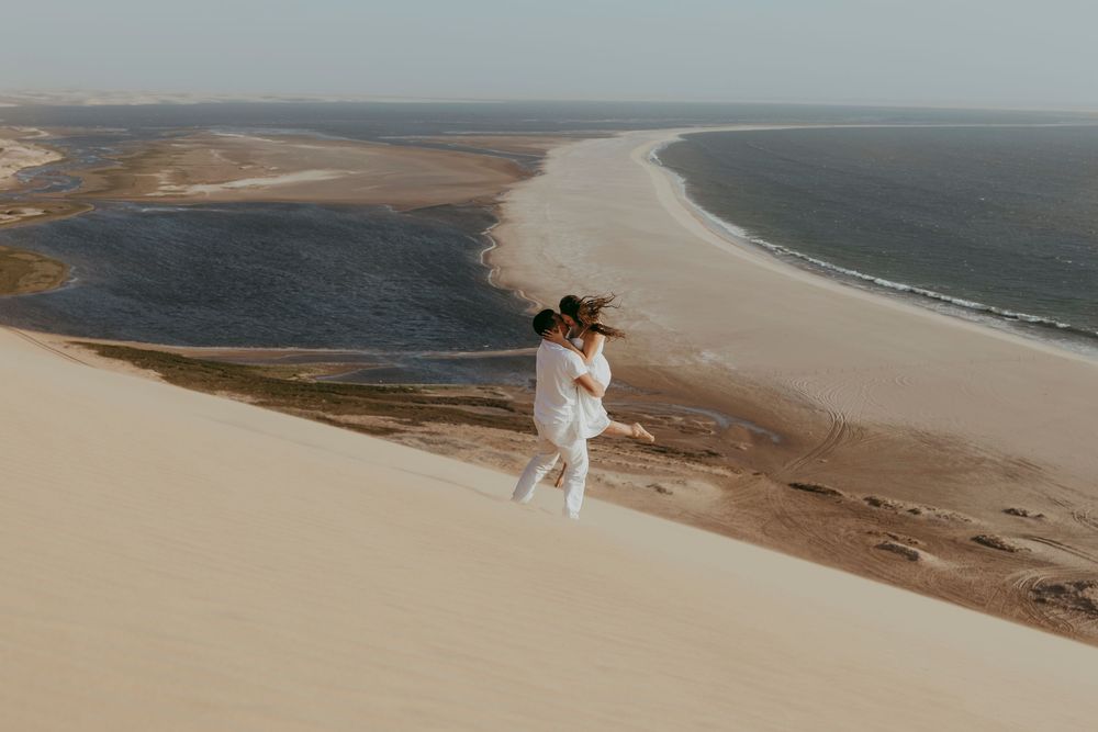 Newly engaged couple hugging at Sandwich Harbour, eyes closed, surrounded by soft sand and warm Namibian light.