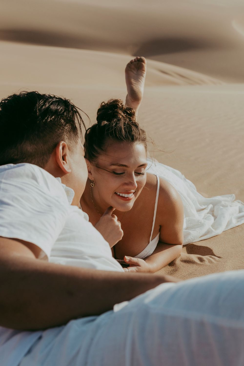 Candid close-up of a US couple laughing during their Sandwich Harbour photoshoot, golden dunes glowing around them.