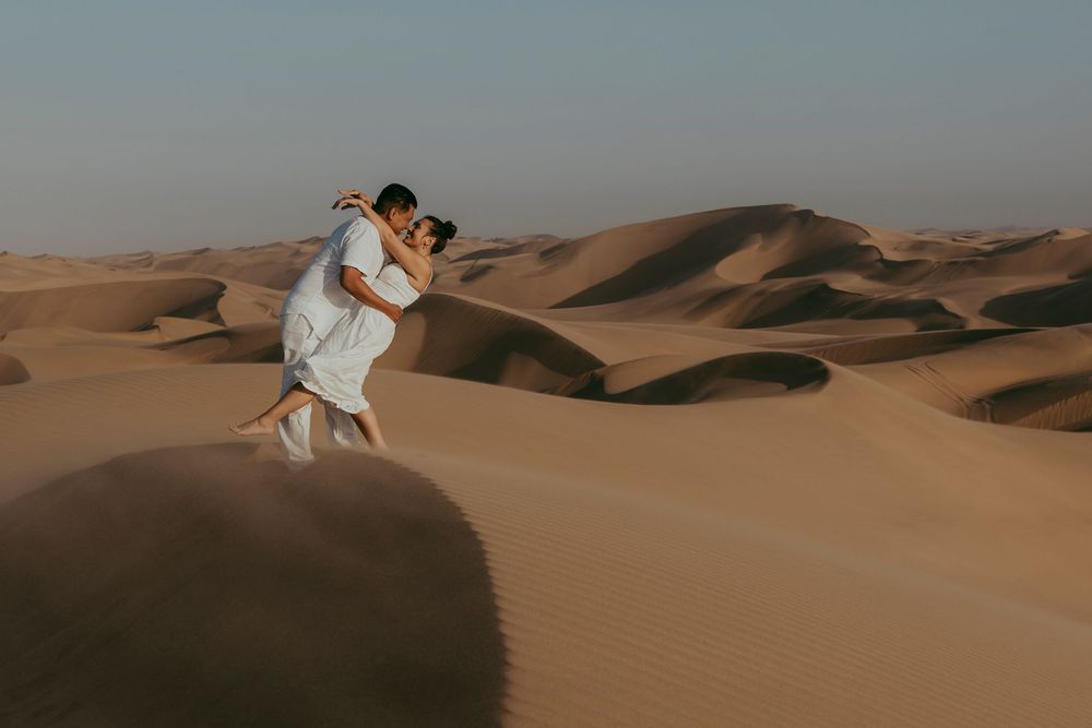 Newly engaged couple hugging at Sandwich Harbour, eyes closed, surrounded by soft sand and warm Namibian light.