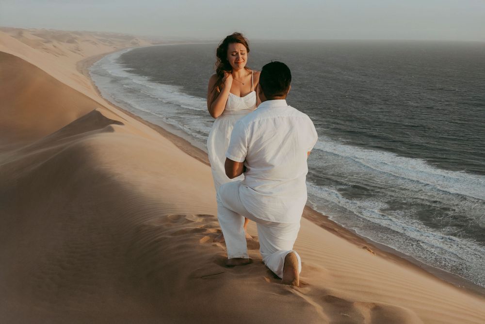 A surprise proposal unfolding on top of a dune in Sandwich Harbour, with the woman reacting emotionally as the sun sets behind them.