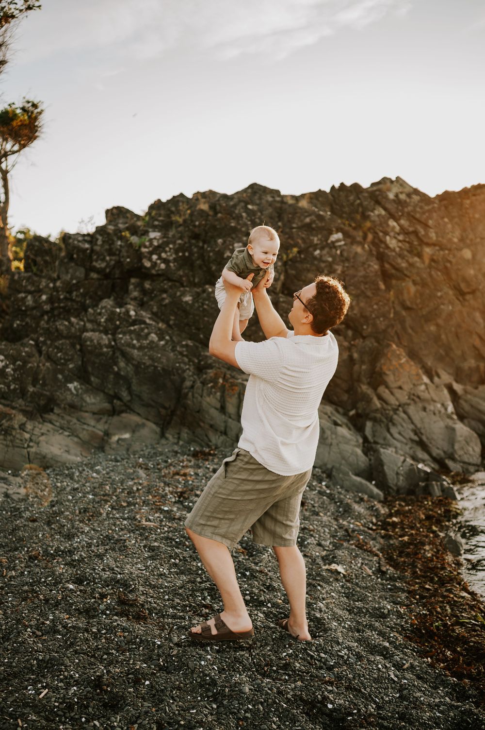 Family photo of dad holding baby in air beach at Neck Point Park Nanaimo golden hour family photography by Vancouver Island photographer