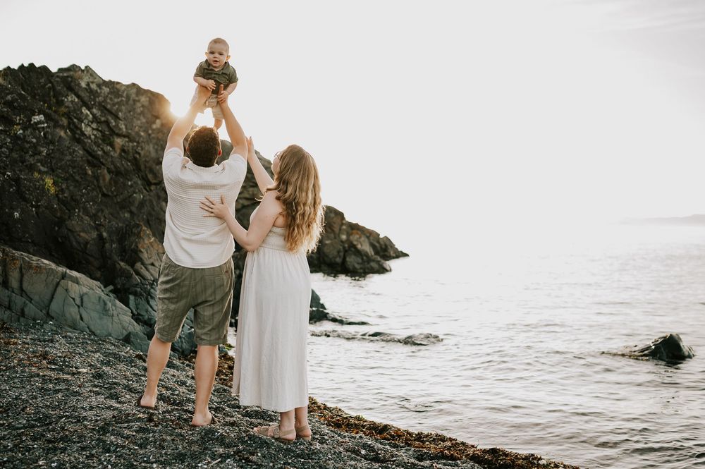 Family photo of parents holding baby in air beach at Neck Point Park Nanaimo golden hour family photography by Vancouver Island photographer
