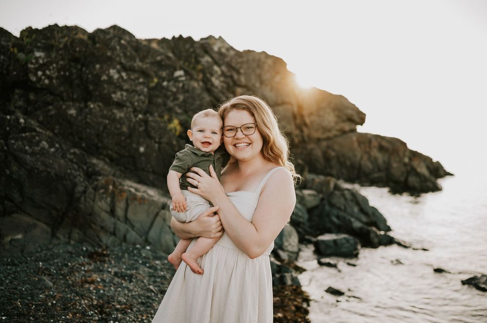 Family photo of mom smiling with baby on beach at Neck Point Park Nanaimo golden hour family photography by Vancouver Island photographer