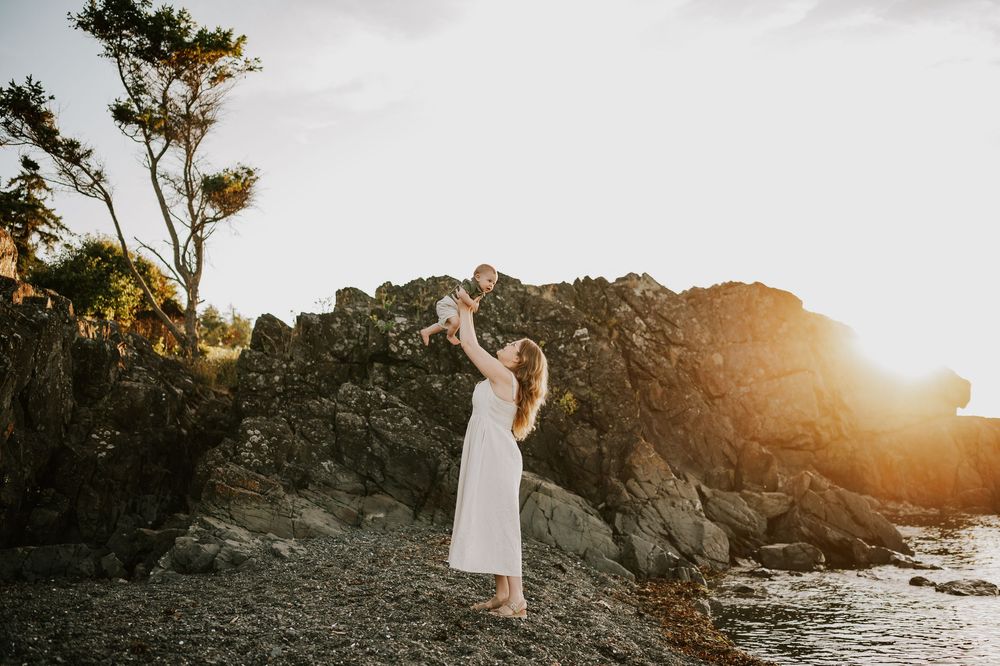 Family photo of mom holding baby in air beach at Neck Point Park Nanaimo golden hour family photography by Vancouver Island photographer