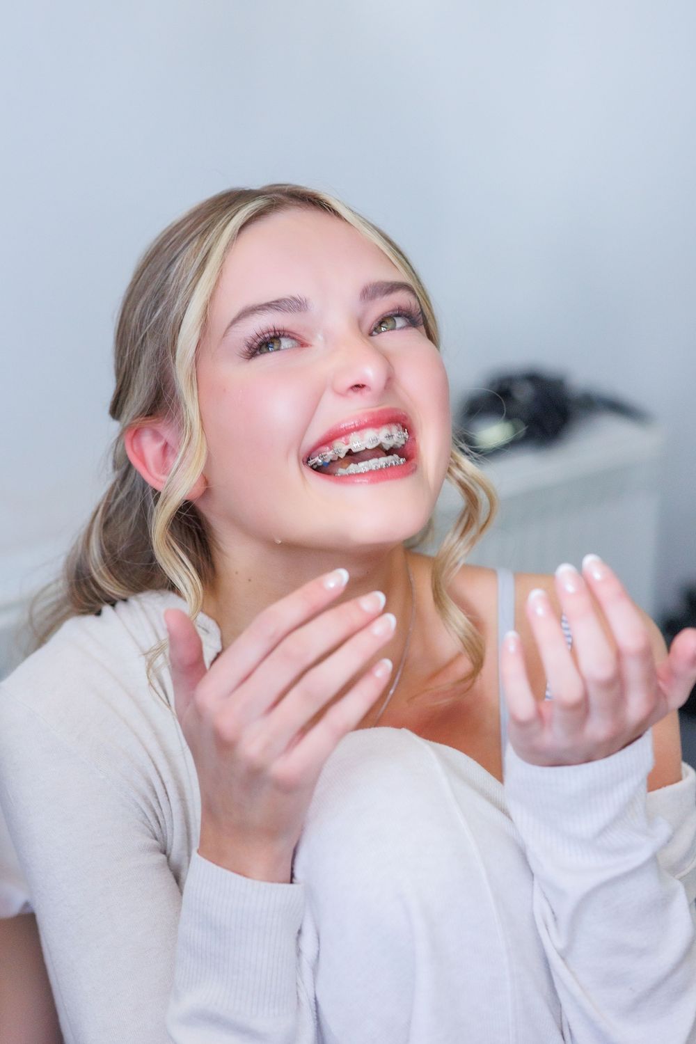 Woman wearing beige sweater laughing joyfully with hands raised close to her face.