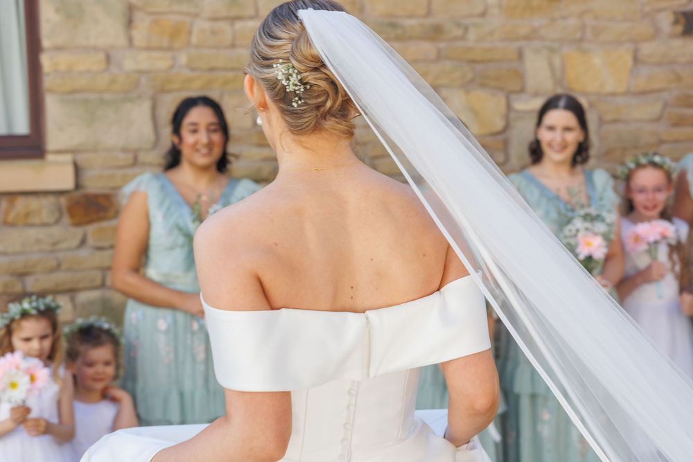 A line of bridesmaids in mint green dresses holding white bouquets walk down stone hallway during wedding ceremony.