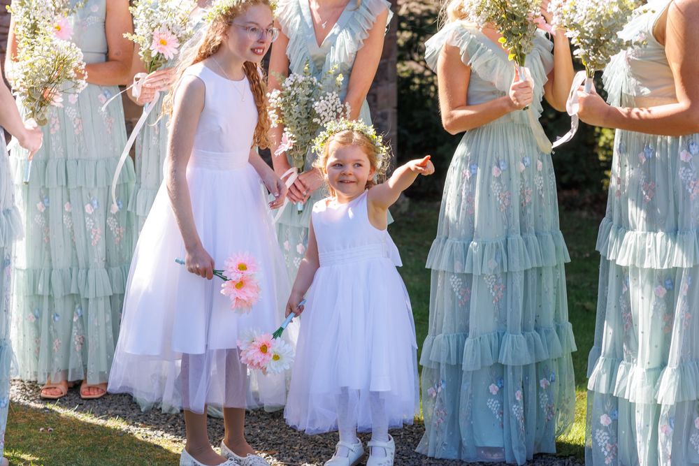 Bridesmaids in flowing mint-colored tiered dresses stand alongside white-dressed attendants at an outdoor wedding ceremony.