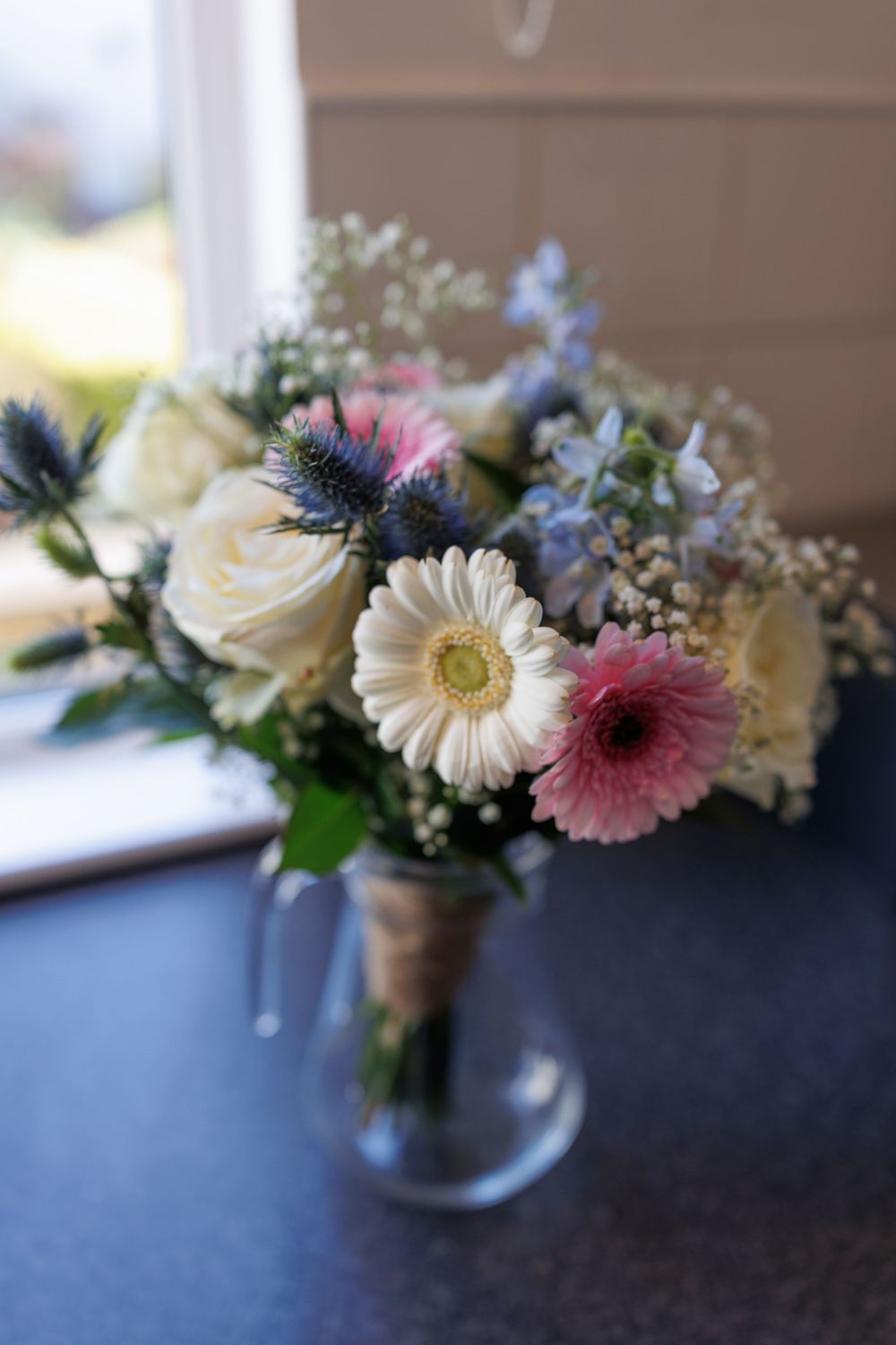Wedding bouquet with white roses, pink gerberas, and blue thistle flowers in rustic style.