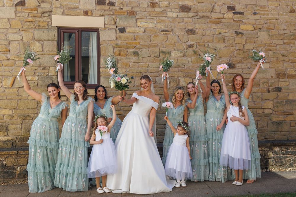 Wedding party in mint green bridesmaid dresses and white flower bouquets pose against stone wall.