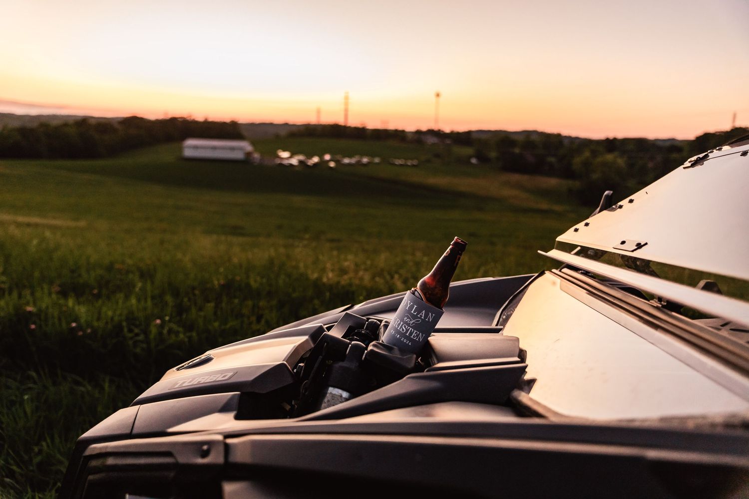 A car sits on the side of a rural road at sunset while silhouettes of grass and fields stretch into the horizon.