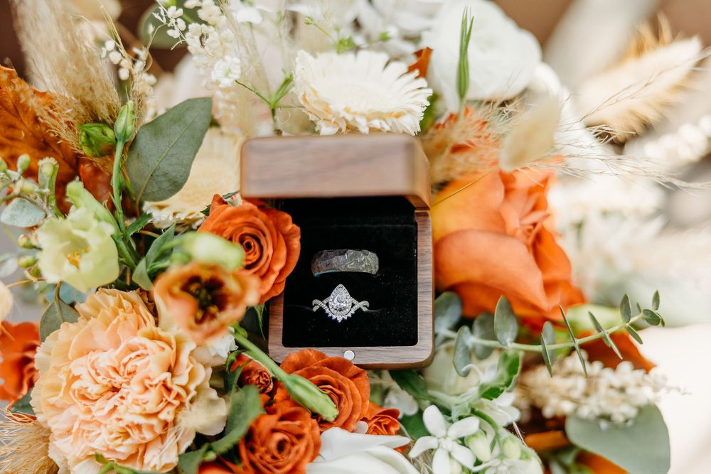 Engagement ring in black box surrounded by peach and coral flowers with eucalyptus.