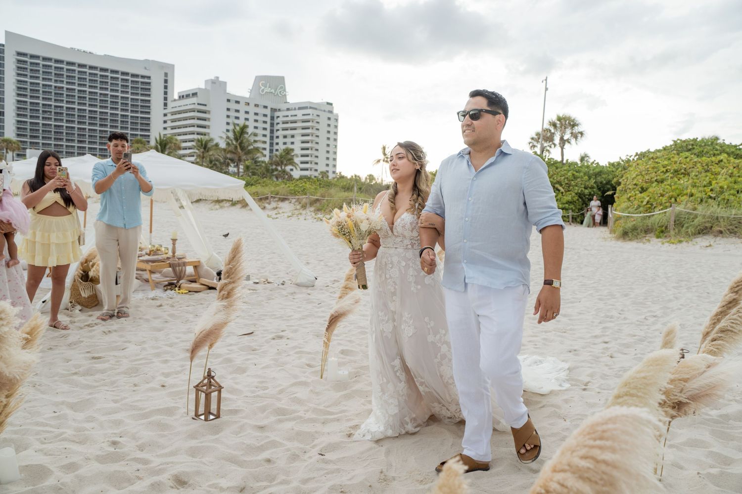 Wedding party walks together on sunny Miami Beach with high-rise hotels in background and seabirds nearby.