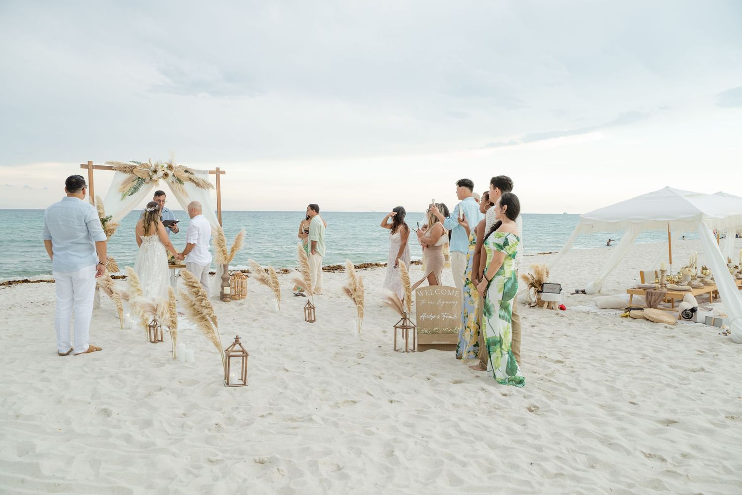 A beachside wedding ceremony with chairs set up on white sand as guests gather near the turquoise ocean waters.