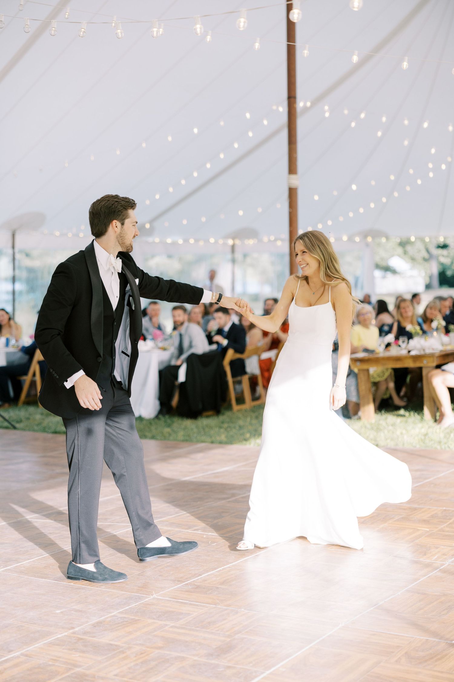 Newlyweds share their first dance under a romantic tent with twinkling lights at an elegant outdoor wedding reception.