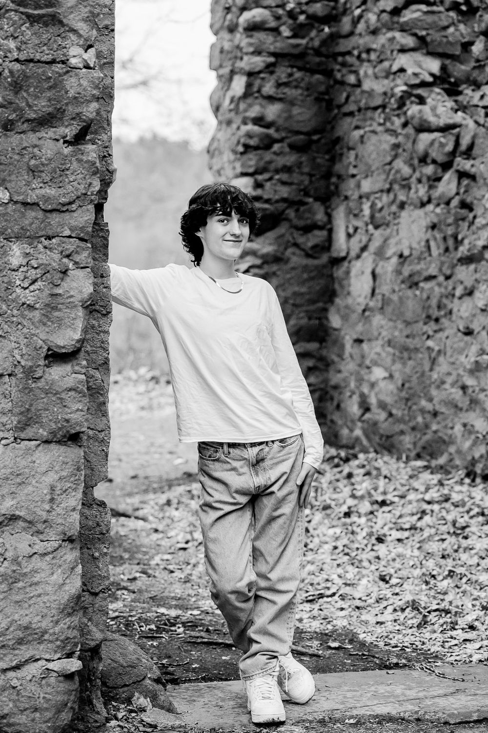 A person in casual white attire poses against ancient stone ruins in a black and white photograph.
