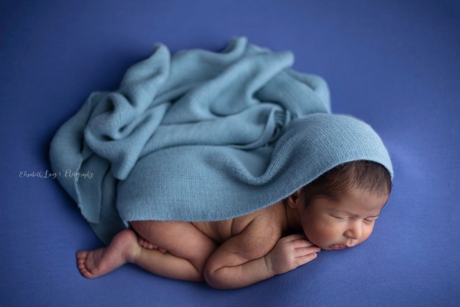 A newborn photography session with video and photos for a fuller experience. Baby boy with blue fabric wraps.