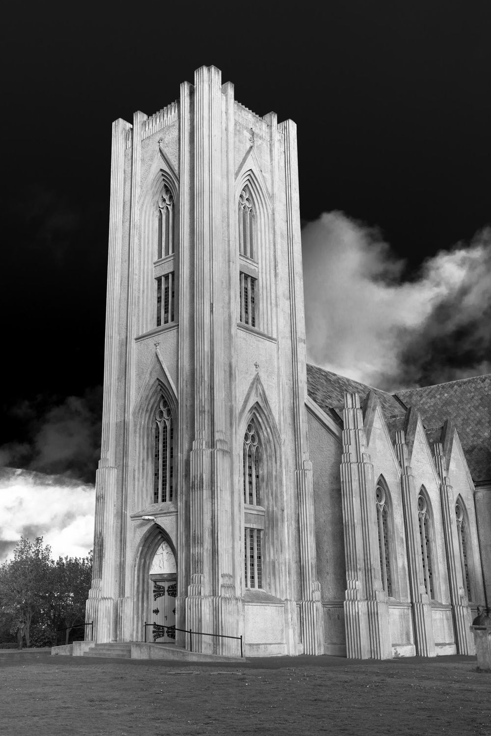 Dramatic black and white photograph of a Gothic church tower with pointed arches against a cloudy sky.