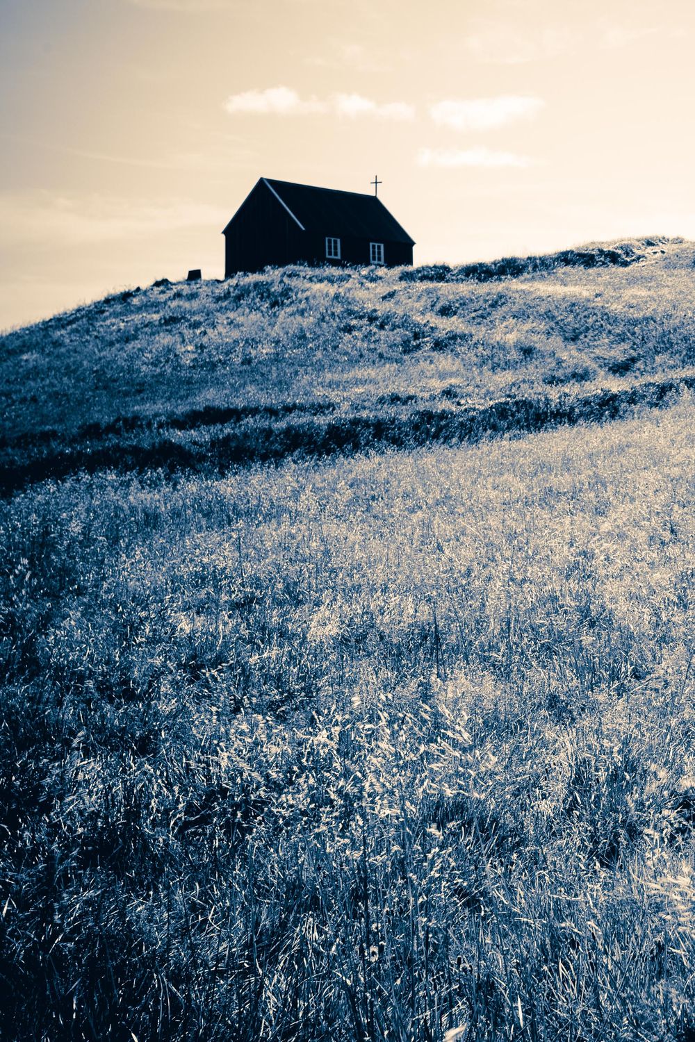 A small black church or chapel sits atop a frosty hillside, silhouetted against a pale winter sky.