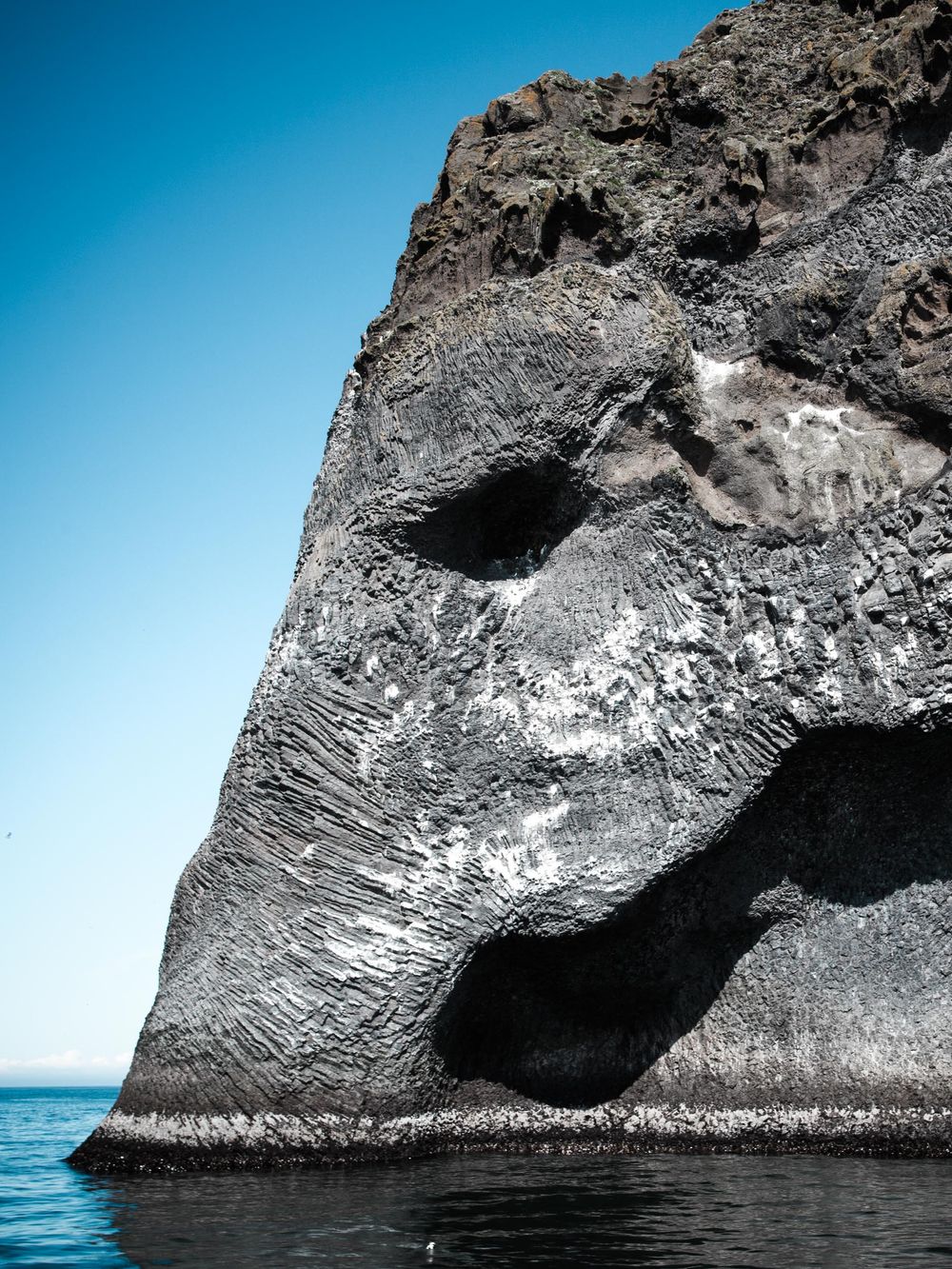 Split view of a dramatic rock formation in the ocean showing geometric patterns and textures against blue water.
