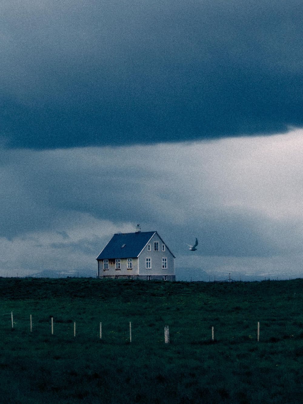 A series of moody photographs showing a solitary house on a rugged coastline under dark stormy skies at dusk.