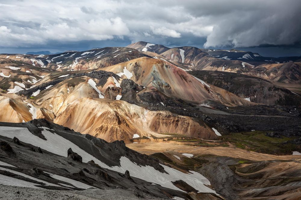 Colorful rhyolite mountains with patches of snow in Landmannalaugar, Iceland under dramatic storm clouds.