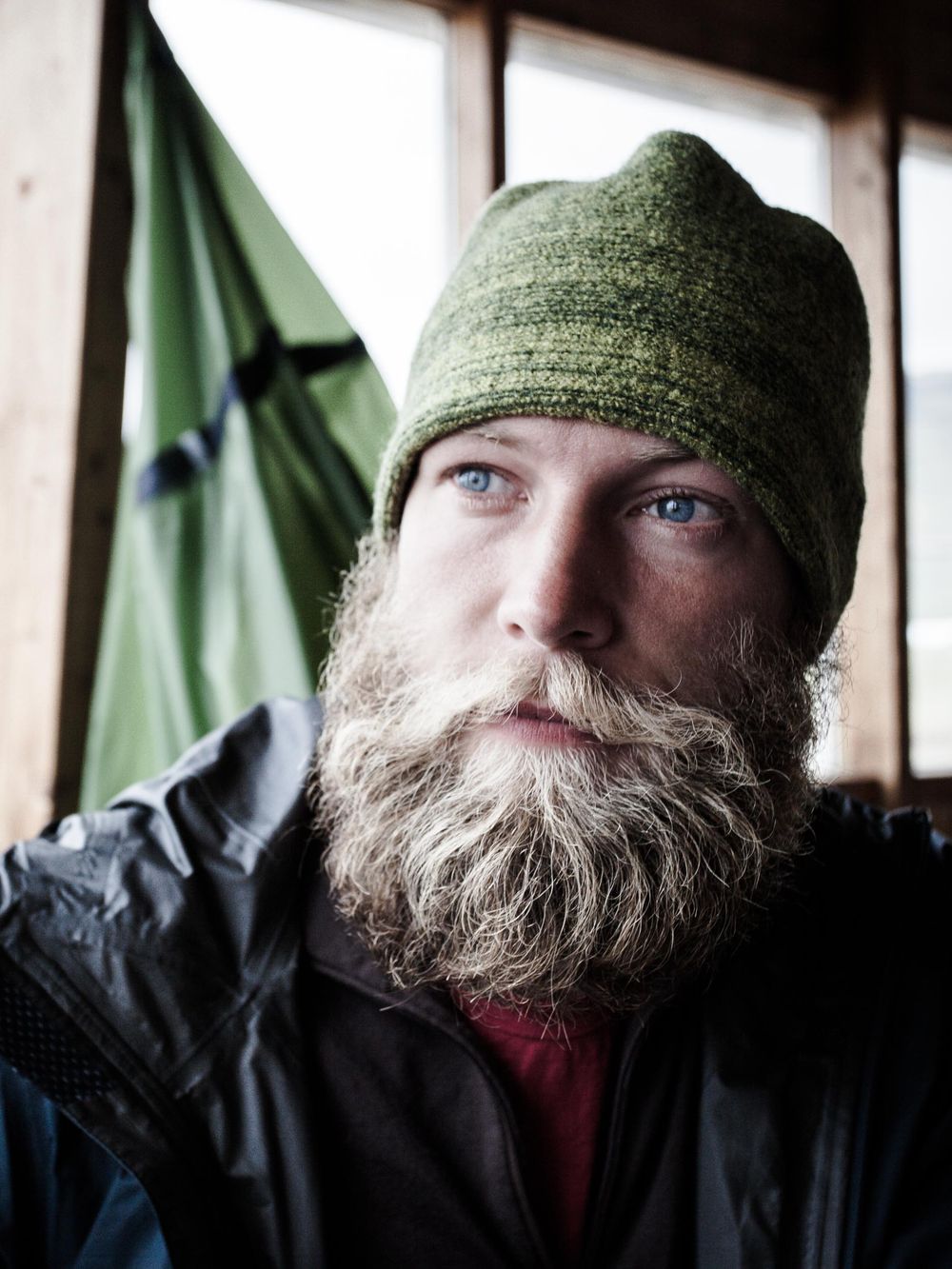 Close up portrait of someone wearing a green beanie and black jacket in front of a green camping tent.