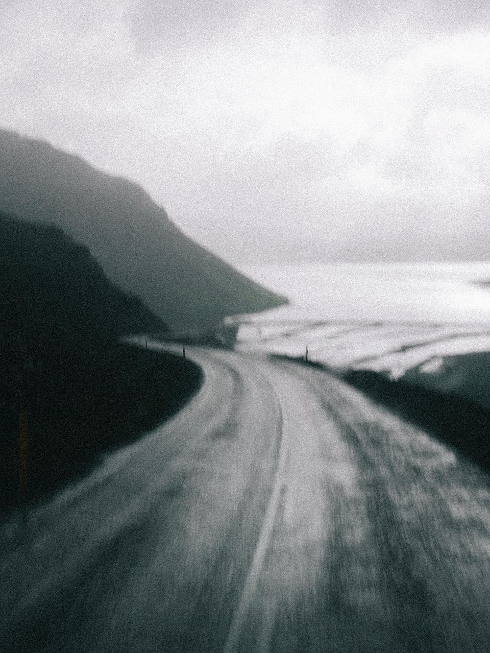 Misty coastal road winding along steep cliffs and ocean waves in moody black and white photography.