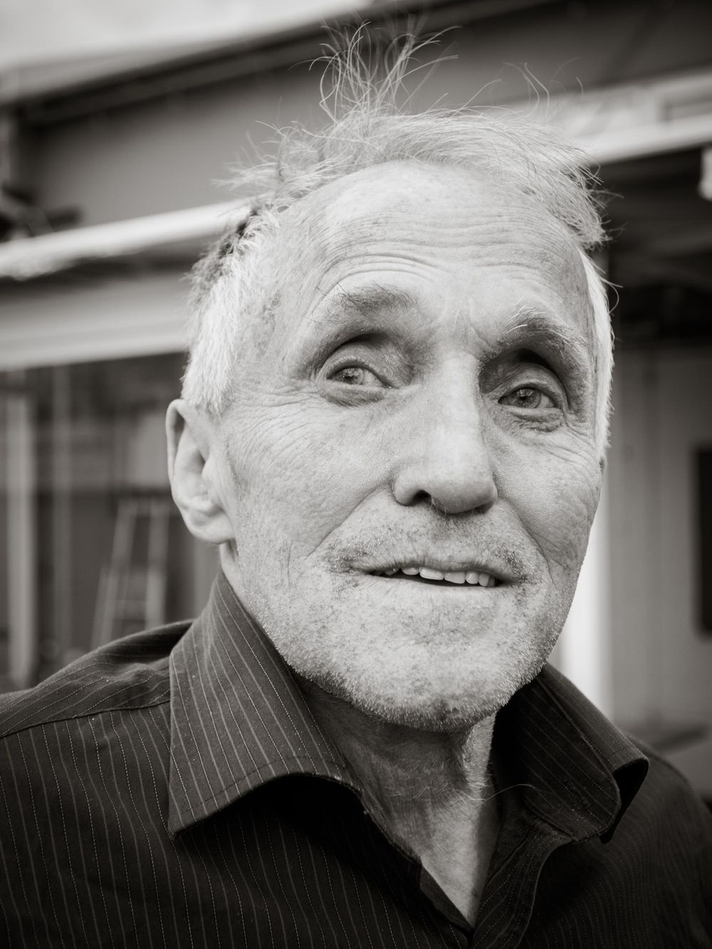 Black and white portrait of an elderly man with gray hair wearing a pinstriped shirt, smiling warmly at the camera.