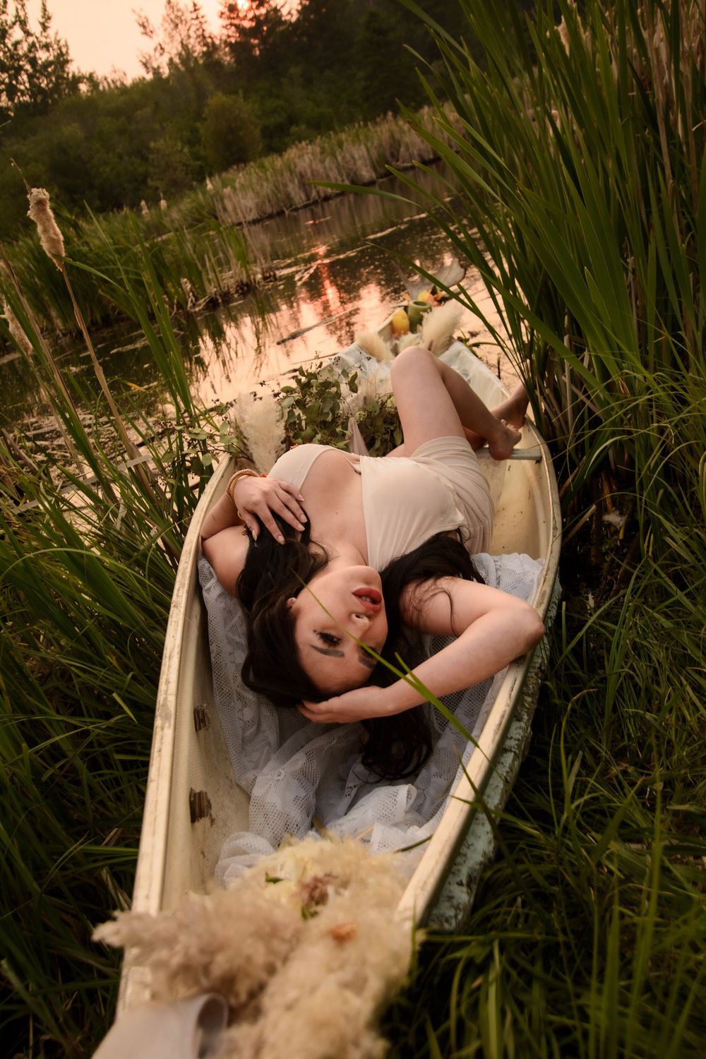 A romantic scene of a person laying in a vintage rowboat among tall reeds during golden hour on a tranquil lake.