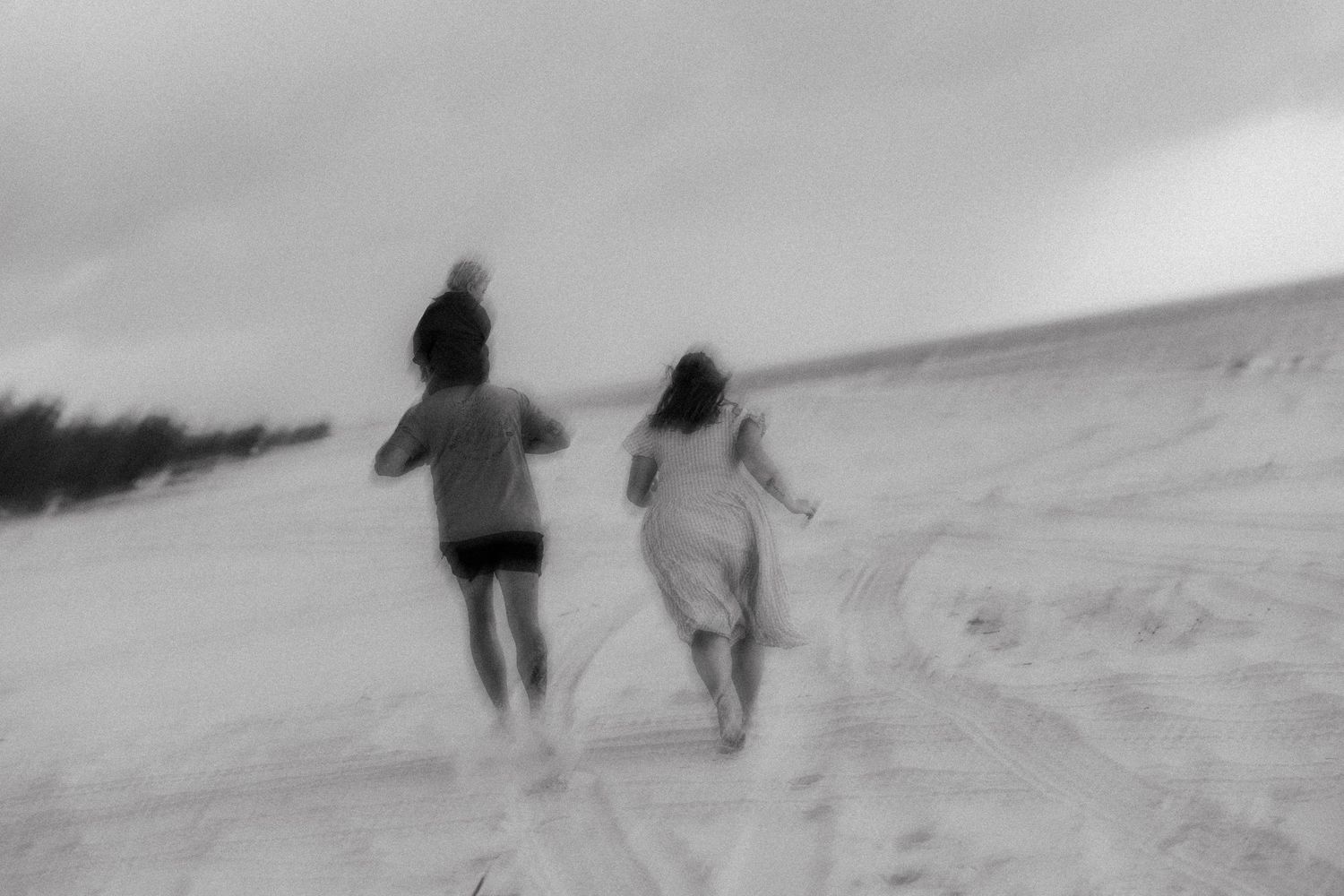 Two blurred figures running together on a sandy beach slope in black and white photography.