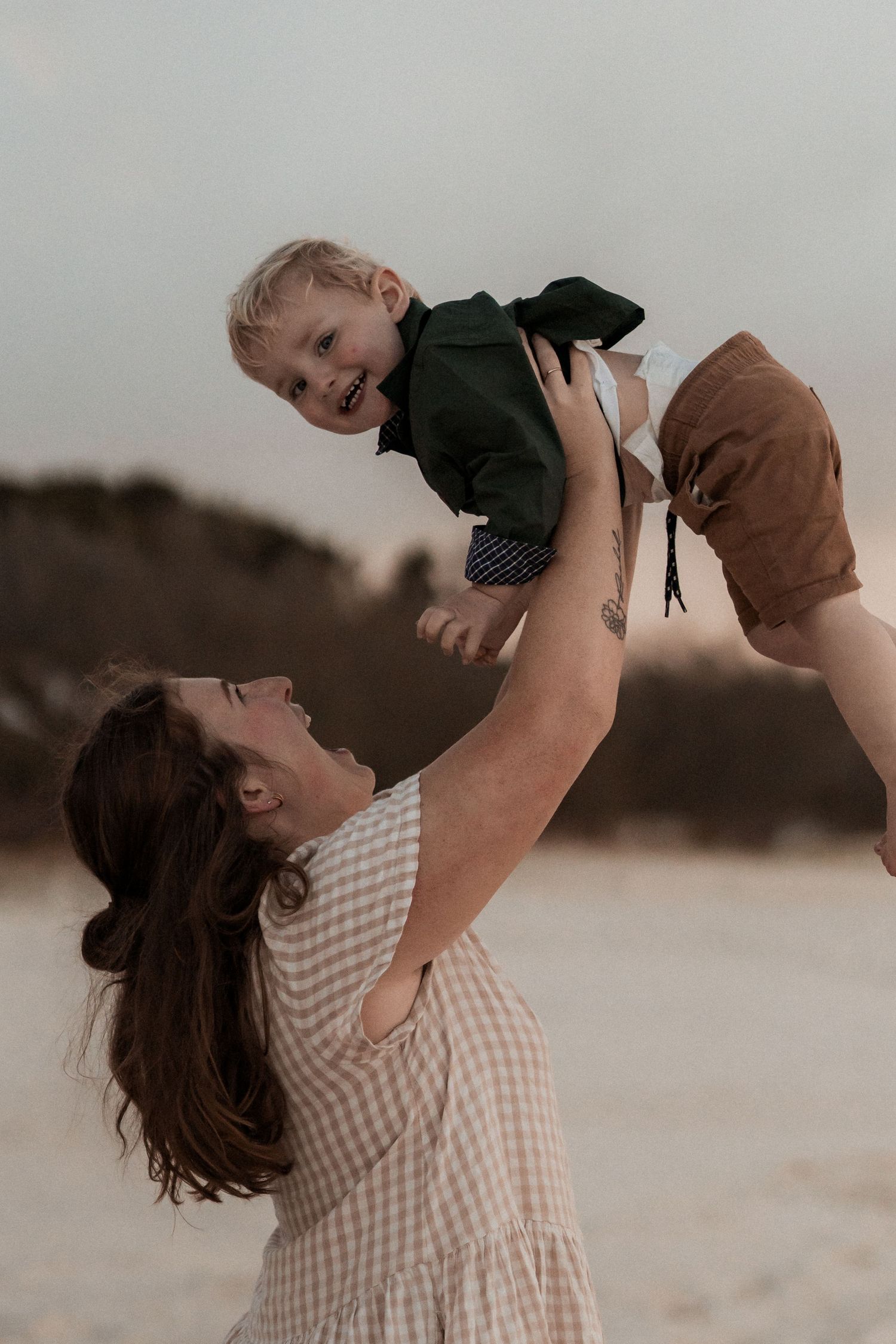 A parent wearing a checkered shirt lifts and plays with a small child outdoors, creating a joyful bonding moment.