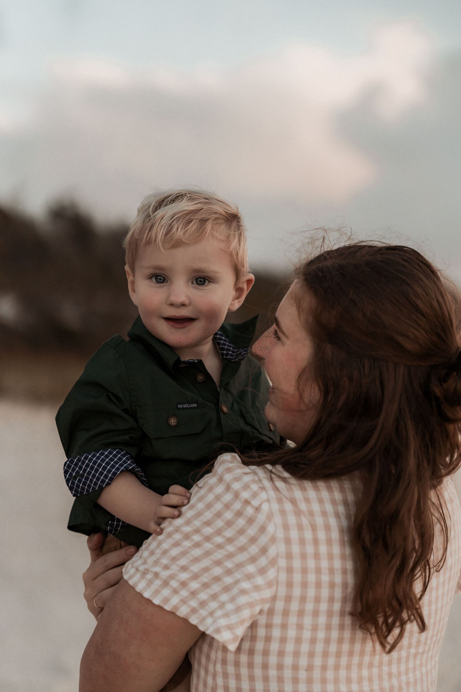 A tender moment between parent and child outdoors at dusk, with the youngster wearing a green jacket.