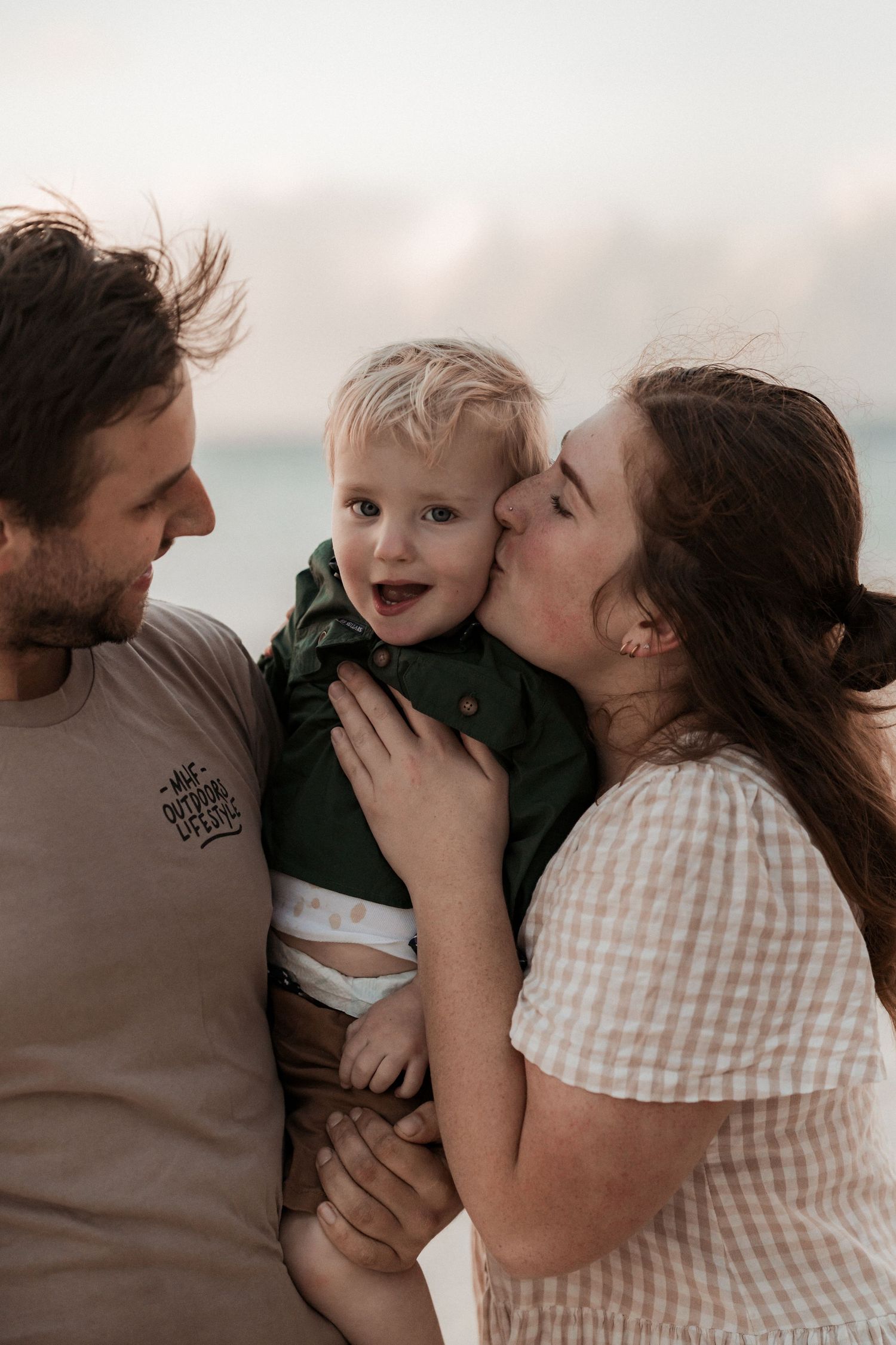 A warm family moment captured outdoors at sunset with parents lovingly embracing their young child.