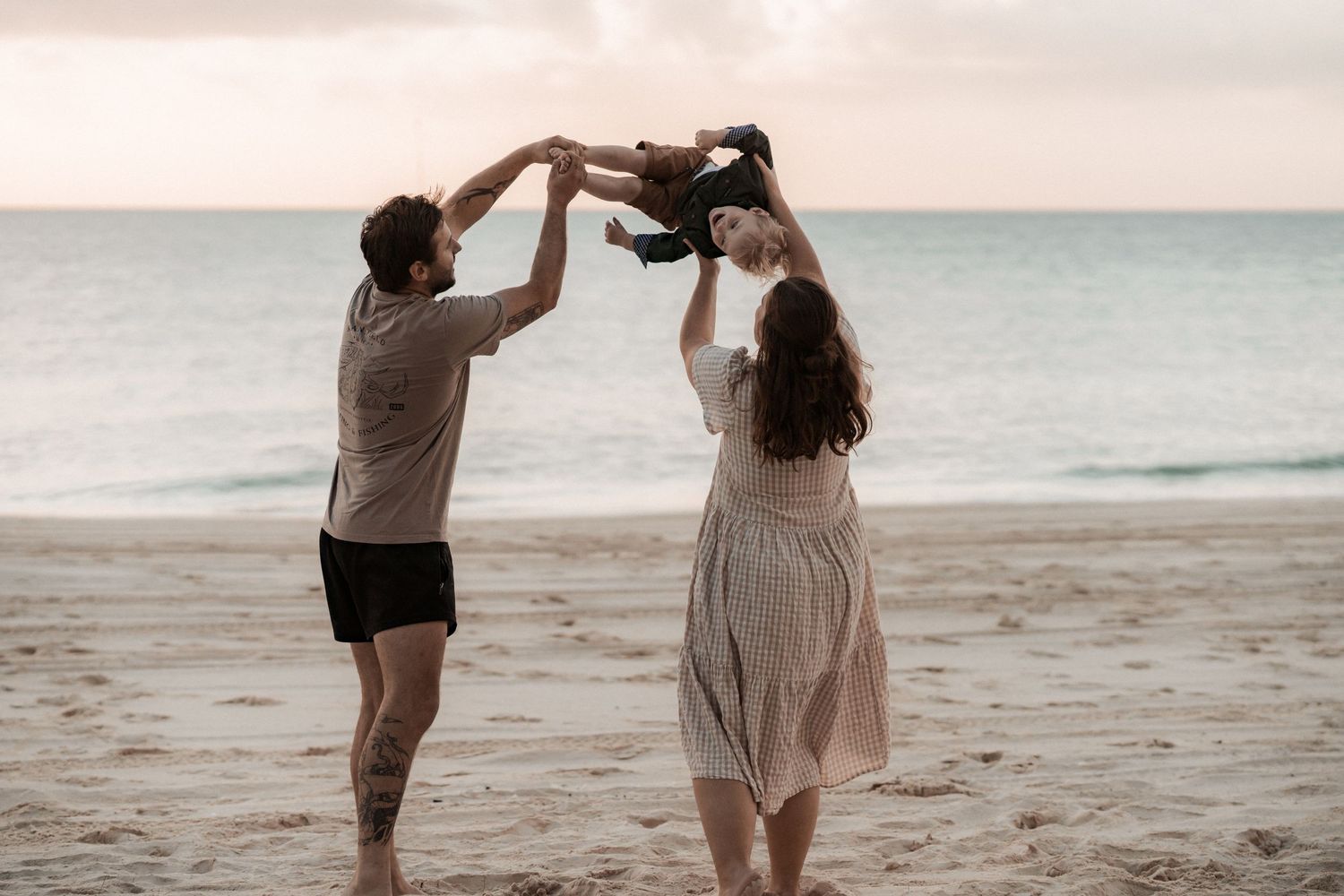 Two people dance together on a peaceful beach during sunset while holding hands and twirling.